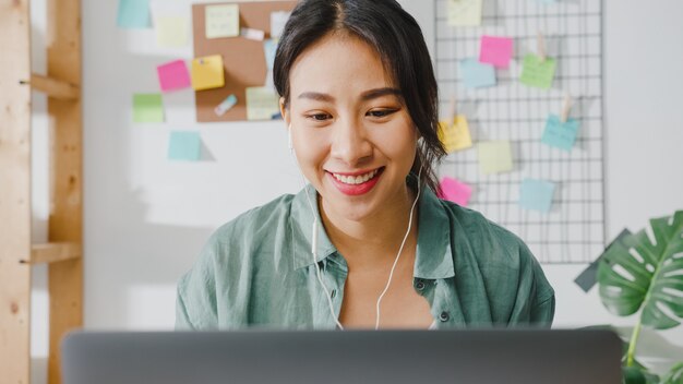 Asia businesswoman using laptop talk to colleagues about plan in video call while smart working from home at living room.