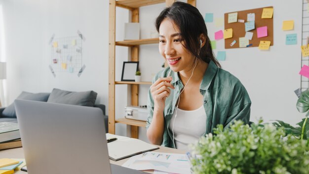 Asia businesswoman using laptop talk to colleagues about plan in video call while smart working from home at living room.