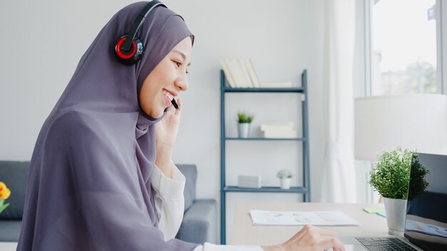 Asia muslim lady wear headphone watch webinar listen online course communicate by conference video call at house.