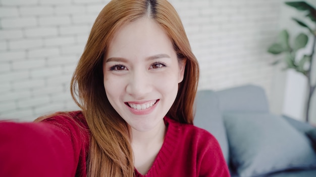 Asian blogger woman using smartphone recording vlog video in living room at home