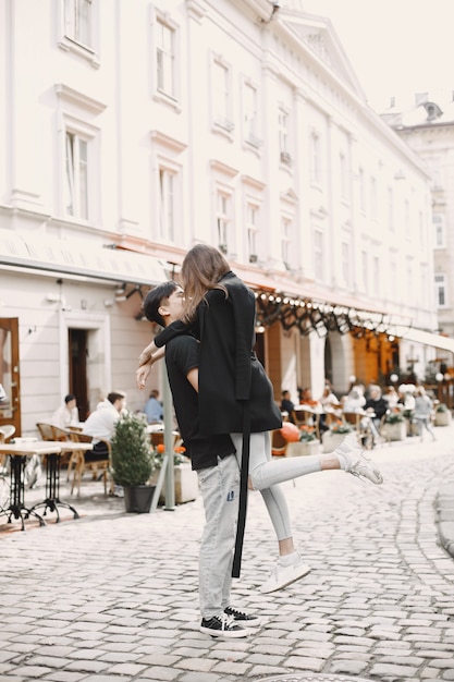 Asian boy and his caucasian girlfriend in casual wear standing on Lviv street. Couple hugging each other while walking together in city