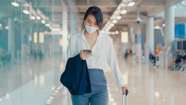 asian business girl using smartphone for check boarding pass walking with luggage to terminal at domestic flight at airport.