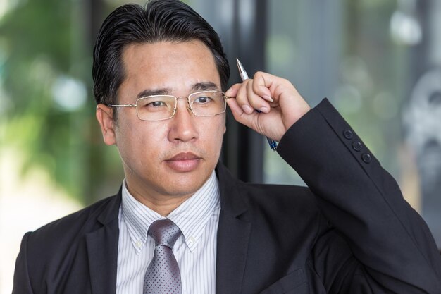 Asian businessman in suit touching adjust glasses with pen