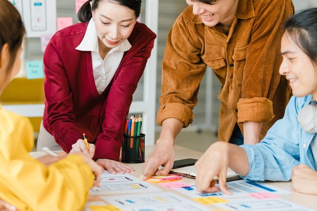 Asian businessmen and businesswomen meeting brainstorming ideas about creative web design planning application and developing template layout for mobile phone project working together in small office.