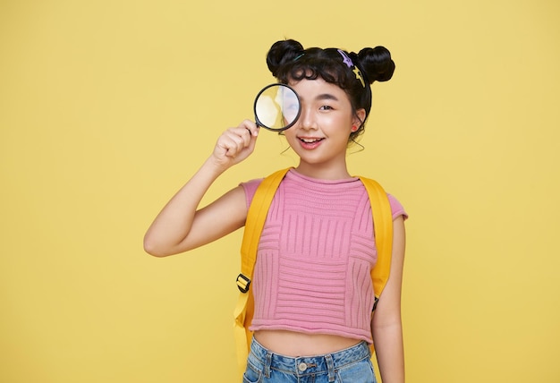 Asian child girl student holding magnifying glass and looking at camera with curious expression