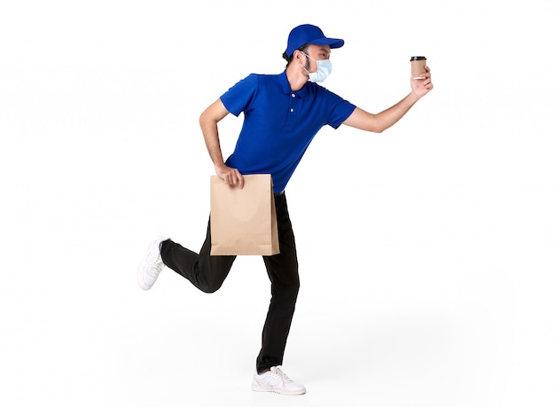 Asian delivery man wearing face mask in blue uniform running with paper bag and takeaway coffee isolated over white space. express delivery service during covid19.