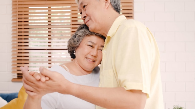 Free photo asian elderly couple dancing together while listen to music in living room at home, sweet couple enjoy love moment while having fun when relaxed at home.