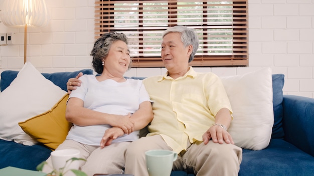 Free photo asian elderly couple feeling happy smiling and looking to camera while relax on the sofa in living room at home.