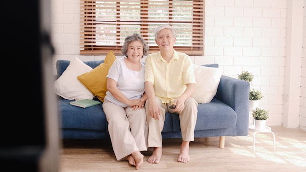 Free photo asian elderly couple watching television in living room at home, sweet couple enjoy love moment while lying on the sofa when relaxed at home.