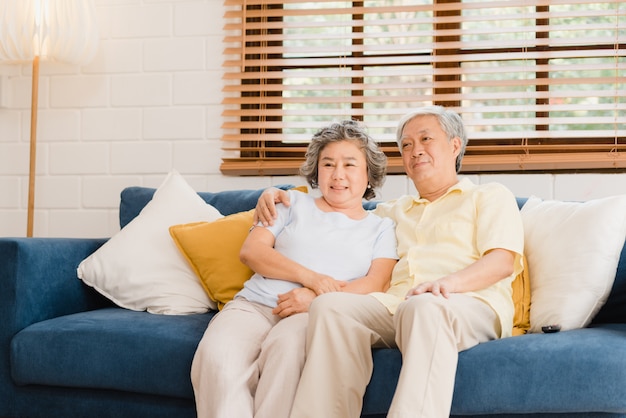 Free photo asian elderly couple watching television in living room at home, sweet couple enjoy love moment while lying on the sofa when relaxed at home.