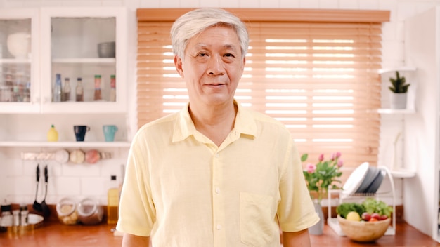 Free photo asian elderly man feeling happy smiling and looking to camera while relax in kitchen at home.