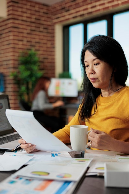 Asian entrepreneur woman holding clipboard with marketing statistics working at business strategy in startup office. Executive manager analyzing graphs, brainstorming ideas for company increase