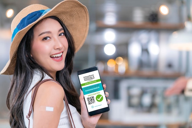 Asian female cheerful smiling teenager hand gesture point show vaccine brand against covid19 and digital vaccine passport from smartphone screen after getting vaccine prevent health concept