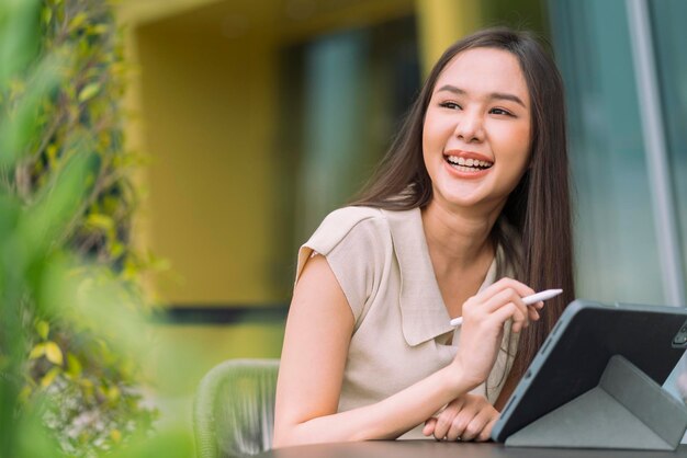 Asian female digital nomad happiness freedom cheerful smiling working using tablet in garden outdoorasia woman freelance relax leisure working anywhere work and travel iwith garden bokeh background