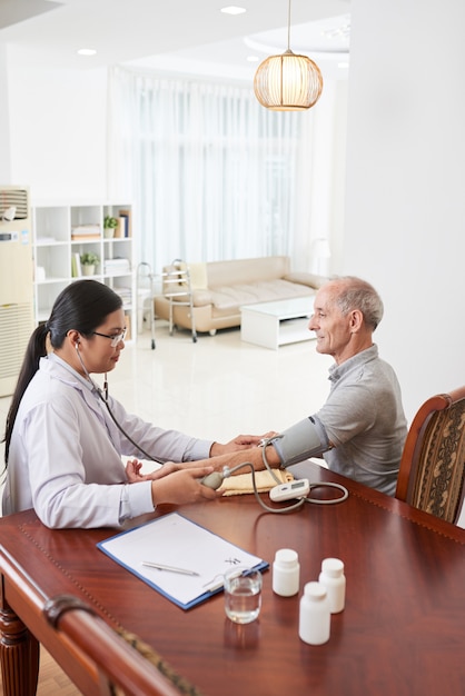 Asian female doctor measuring patient's blood pressure during house call