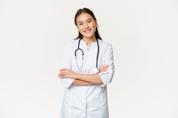 Asian female doctor, physician in medical uniform with stethoscope, cross arms on chest, smiling and looking like professional, white background