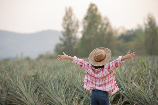 Asian female farmer see growth of pineapple in farm, Young pretty farmer girl standing on farmland with arms raised up joyful elated happiness.