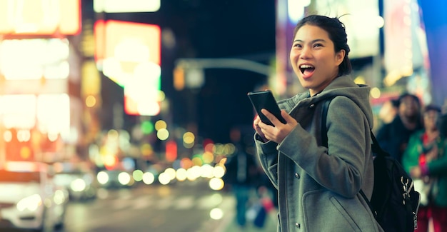 Asian female traveller smile happiness hand hold mirrorless camera enjoy nightlife lifestyle tourost with light bokeh and crowd of people blur background in winter season