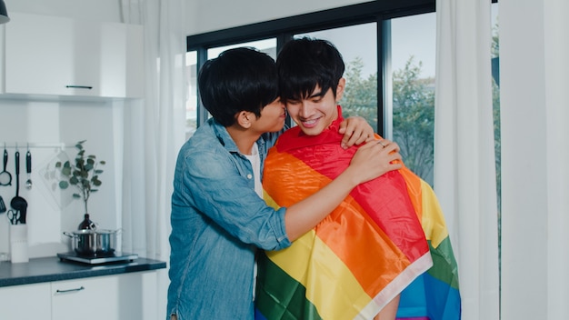 Free photo asian gay couple standing and hugging room at home. young handsome lgbtq+ men kissing happy relax rest together spend romantic time in modern kitchen with rainbow flag at house in the morning .