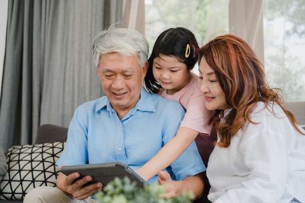 Free photo asian grandparents and granddaughter using tablet at home. senior chinese, grandpa and grandma happy spend family time relax with young girl checking social media, lying on sofa in living room concept