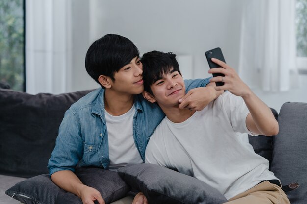 Asian influencer Gay couple vlog at home. Asian LGBTQ men happy relax fun using technology mobile phone record lifestyle vlog video upload in social media while lying sofa in living room .