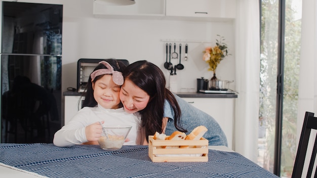 Free photo asian japanese family has breakfast at home. asian mom and daughter feeling happy talking together while eat bread, corn flakes cereal and milk in bowl on table in modern kitchen at house in morning.