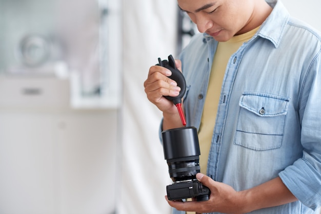 Free photo asian male phographer cleaning camera lens with air blower