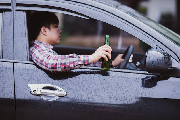 Free photo asian man holds a beer bottle while is driving a car