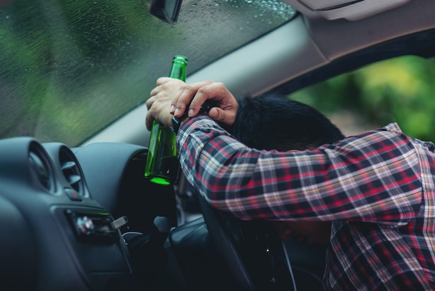 Free photo asian man holds a beer bottle while is driving a car