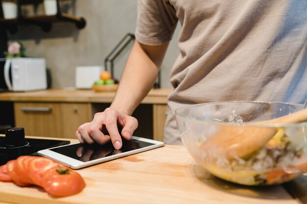 Asian man looking recipe on digital tablet and cooking healthy food in the home kitchen 