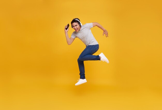 Free Photo asian man smiling holding smartphone and jumping wearing wireless headphone listening to music