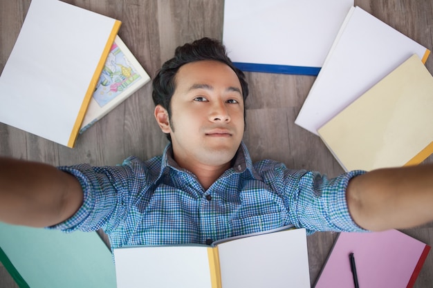 Asian man taking selfie on floor among books