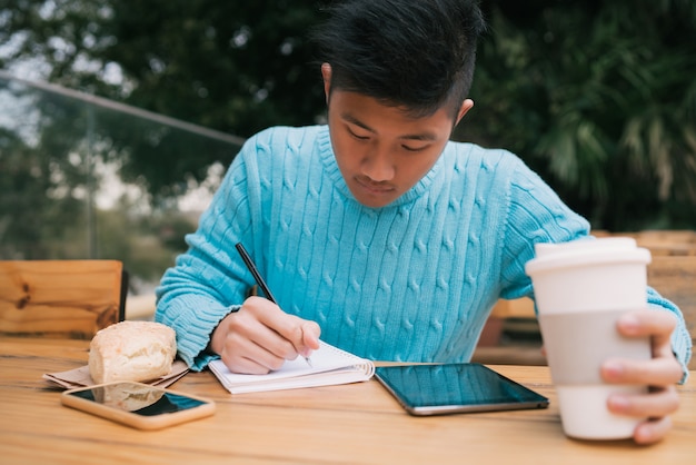 Asian man using digital tablet and taking notes