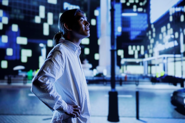 Free Photo asian man wandering around city boulevards during nighttime, being amazed by urban landscape buildings. citizen strolling around empty avenues at night, enjoying street lamps illuminated surroundings