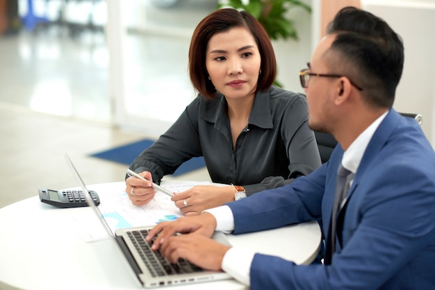 Asian man and woman in business attire sitting at table indoors and talking