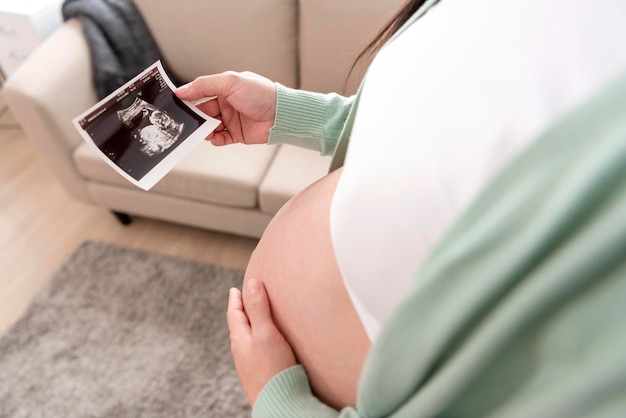 Asian pregnant woman hand holding ultrasound image on belly at home Pregnancy maternity preparation and expectation concept