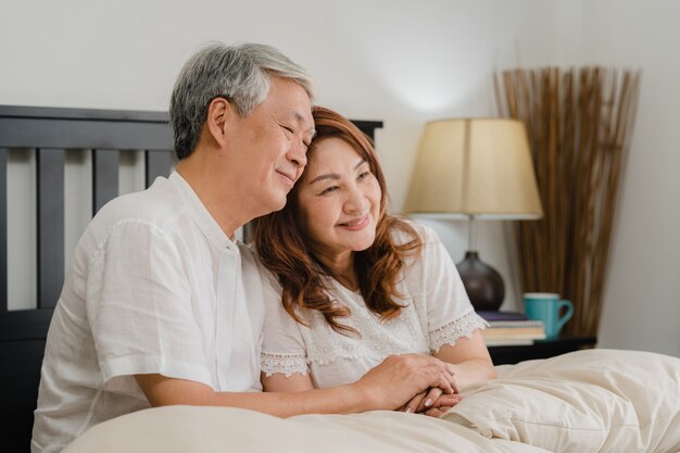 Asian senior couple talking on bed at home. Asian Senior Chinese grandparents, husband and wife happy relax together after wake up while lying on bed in bedroom at home in the morning concept.