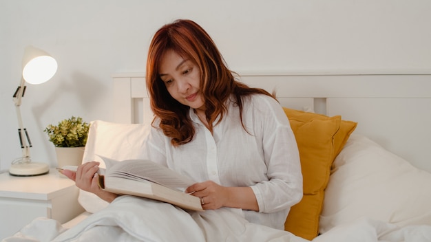 Asian senior women relax at home. Asian Senior Chinese female enjoy rest time read book while lying on bed in bedroom at home at night concept.