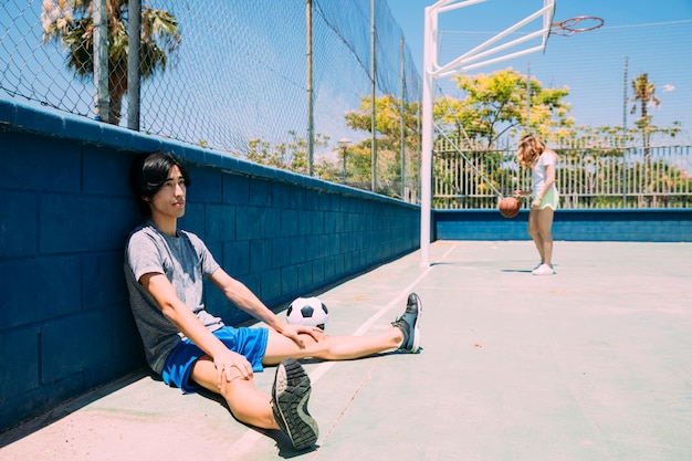 Asian teen student resting beside sportsground fence