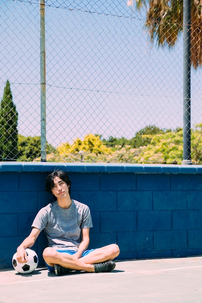 Asian teen student sitting beside sportsground fence