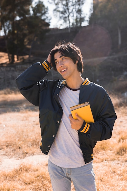 Asian teenager standing with book in park