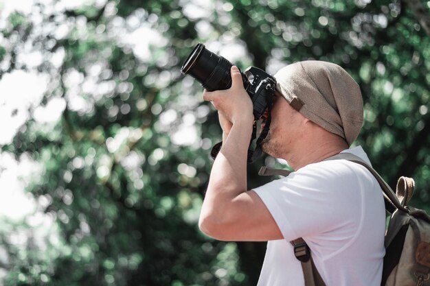 Free photo asian traveler man with backpack taking a photo in the park with copy space travel photographer vocation and holiday concept