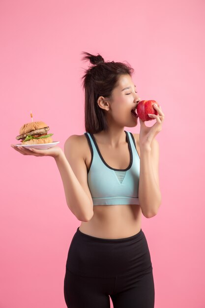 asian woman choosing between hamburger and red apple on pink