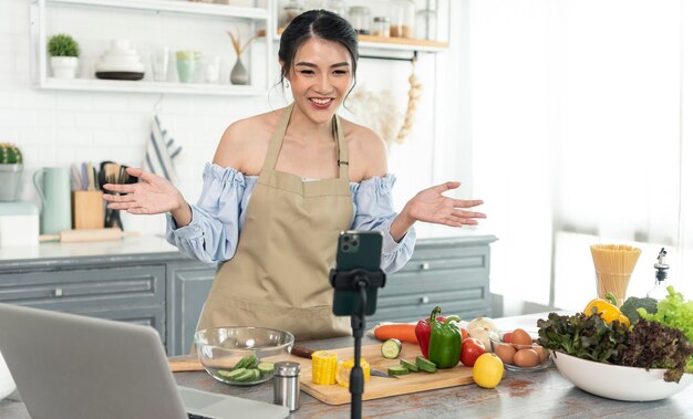 Asian woman food blogger cooking salad in front of smartphone camera while recording vlog video