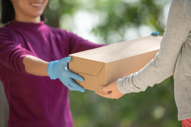 Asian woman from delivery service in purple t-shirt, portrait of delivery man holds cardboard box package standing with customer in front of door at home. home delivery shopping concept.