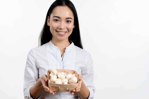 Asian woman holding mushrooms container against white background