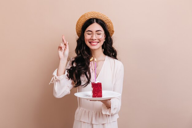 Asian woman making wish with closed eyes. Charming korean woman holding cake with candles.