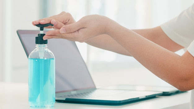 Asian woman using alcohol gel hand sanitizer wash hand before open laptop for protect coronavirus. Female push alcohol to clean for hygiene when social distancing stay at home and self quarantine time