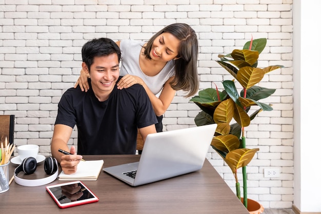 Asian woman wife motivate advice man husband freelancer working at home sitting at desk dining table in living room