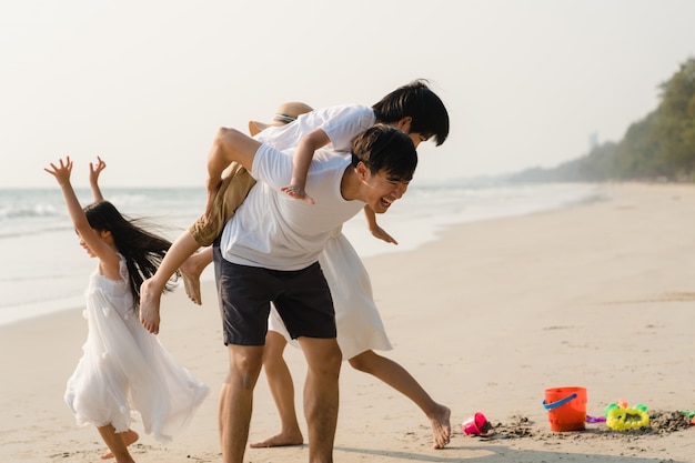 Asian young happy family enjoy vacation on beach in the evening. Dad, mom and kid relax playing together near sea when sunset while travel holiday. Lifestyle travel holiday vacation summer concept.